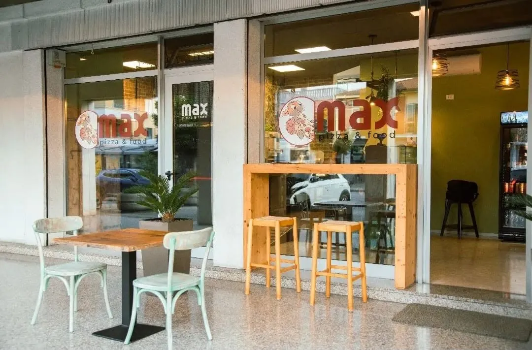 L'ingresso di Max Pizza & Food: vetrine col logo, tavolini e sgabelli all'aperto