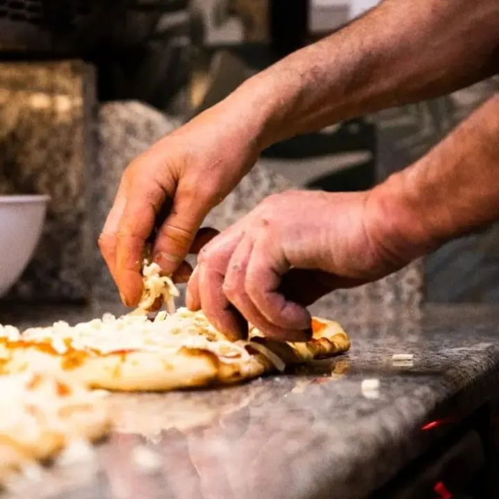 Le mani del pizzaiolo che condiscono una pizza sul bancone