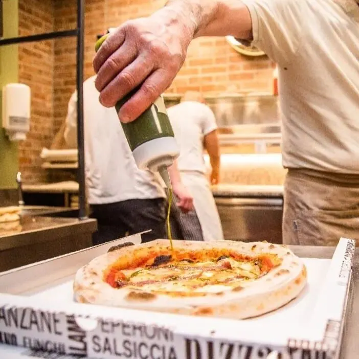 Un filo d'olio su una pizza appena messa nel cartone